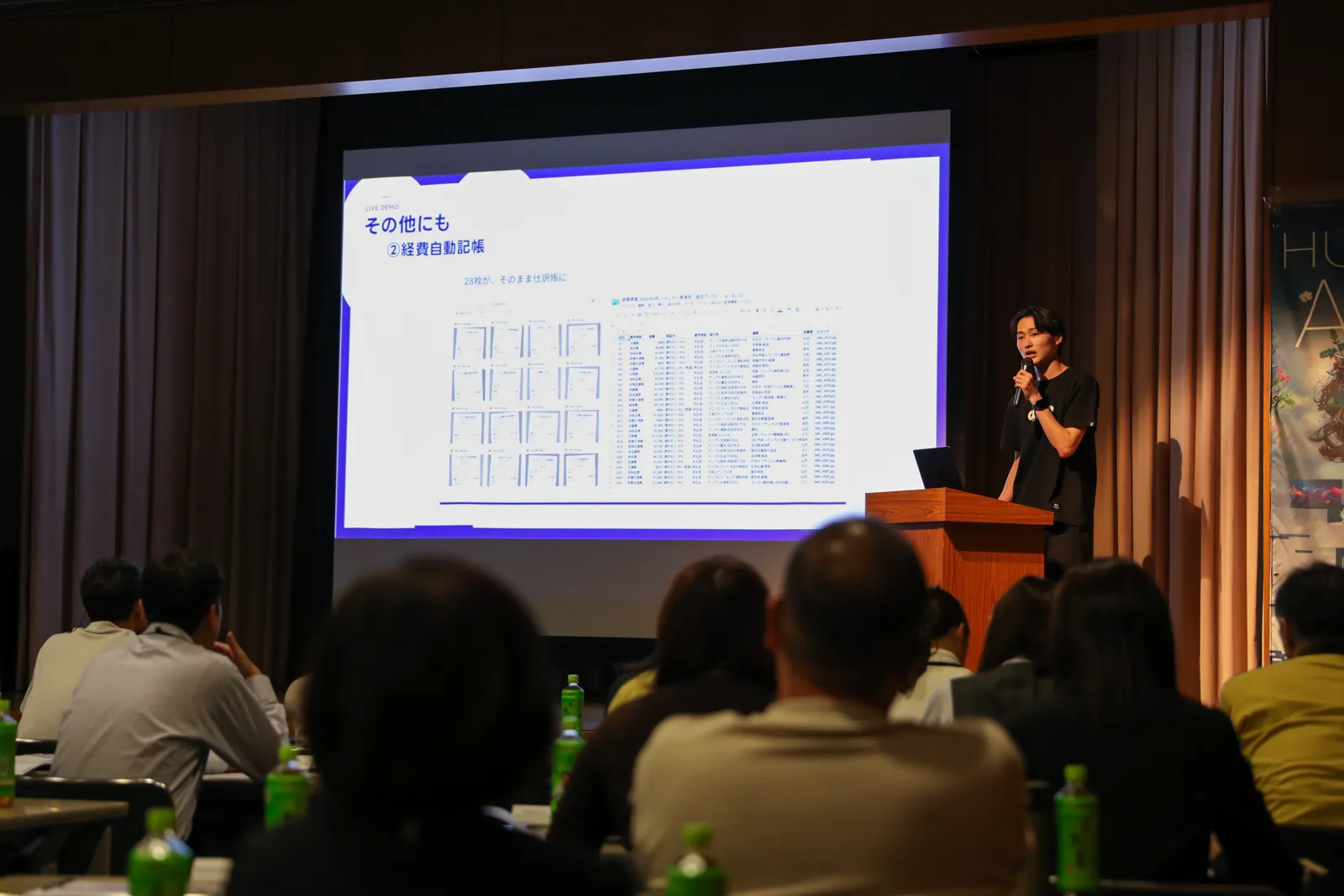 「経費自動記帳」の実演で、28枚のレシートが仕訳帳に自動で記入された画面を映しながら、近藤が解説している様子